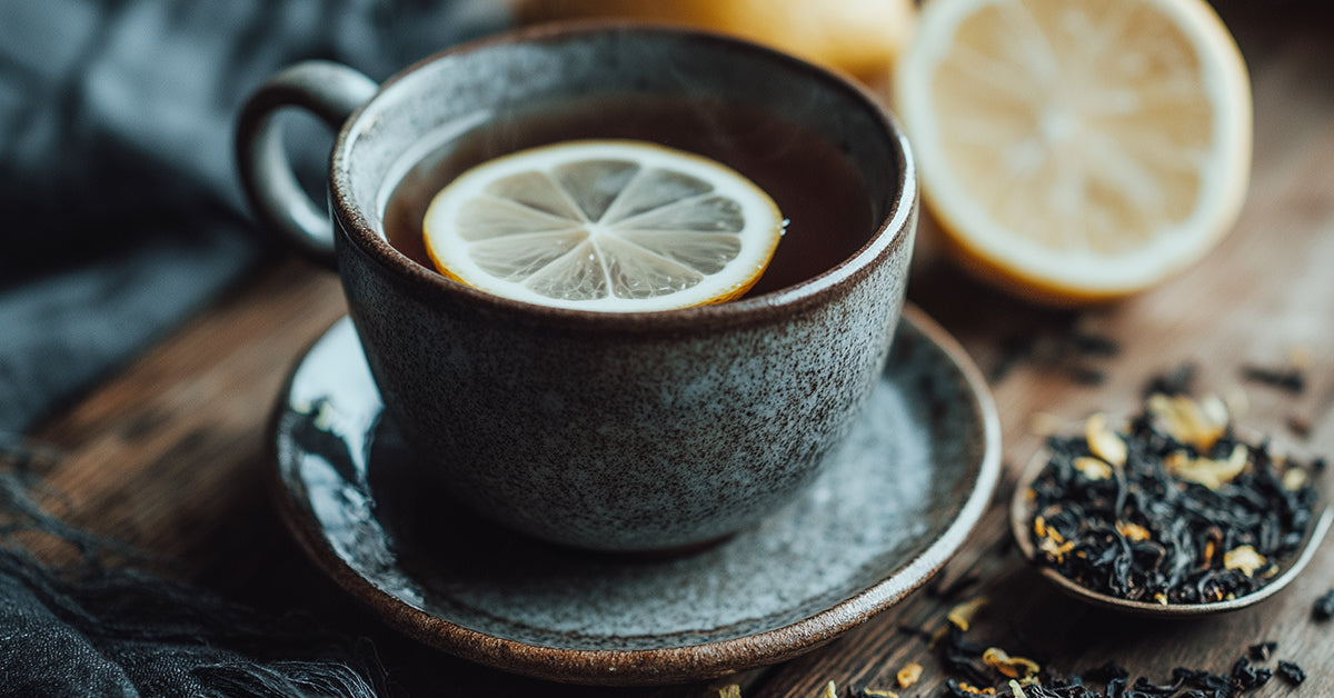 Foto van een kop Earl Grey zwarte thee met een schijfje citroen, losse theebladeren en bergamot op een rustieke houten tafel